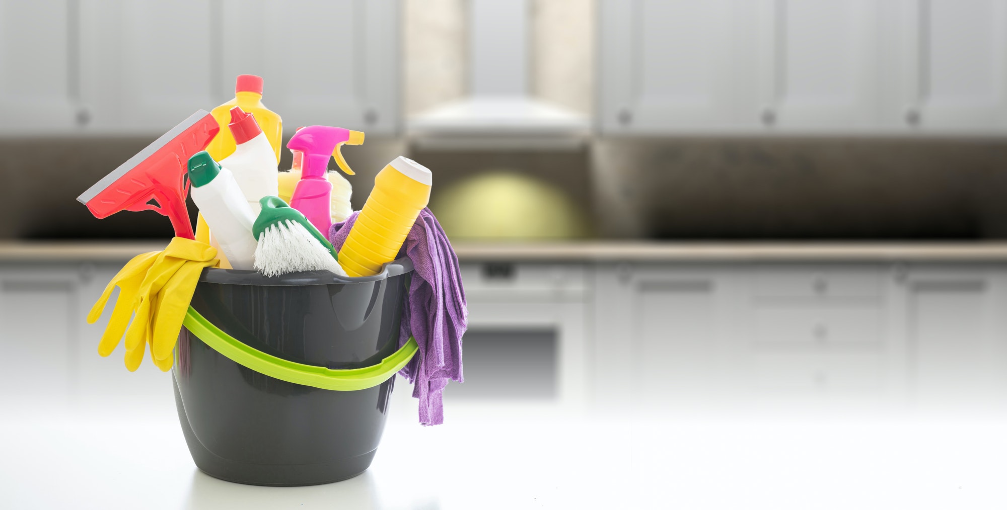 Cleaning supplies in a bucket against blur kitchen cabinets background.